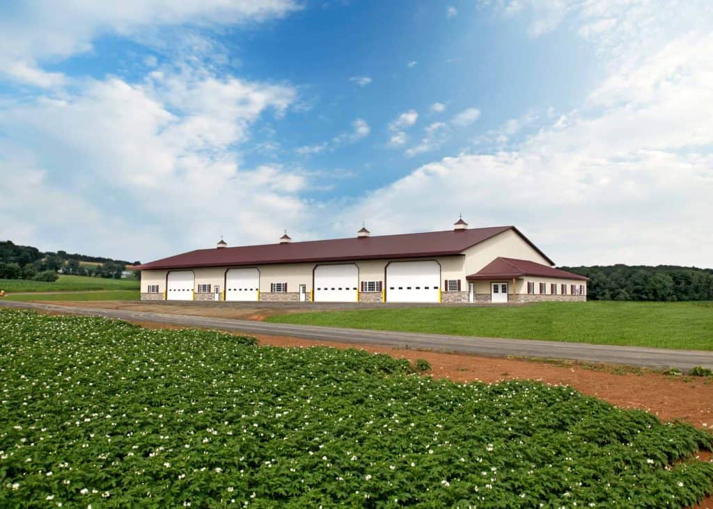 Large modern barn with multiple garage doors, situated on a farm with expansive green fields.