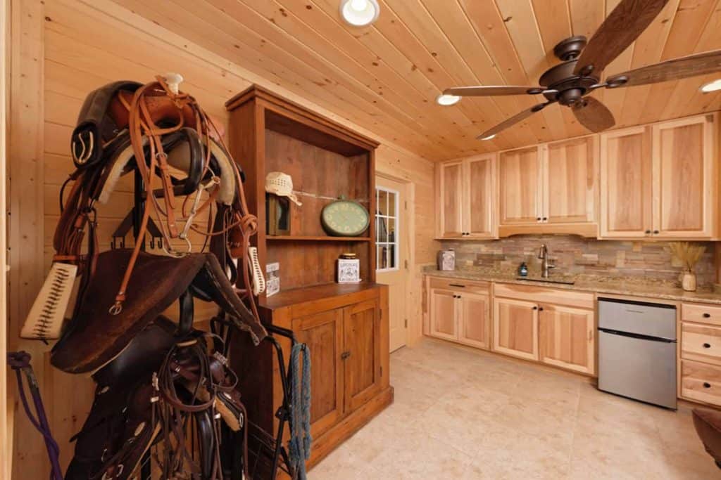 Horse tack and saddle storage area in a cozy rustic kitchen setting with wooden walls.