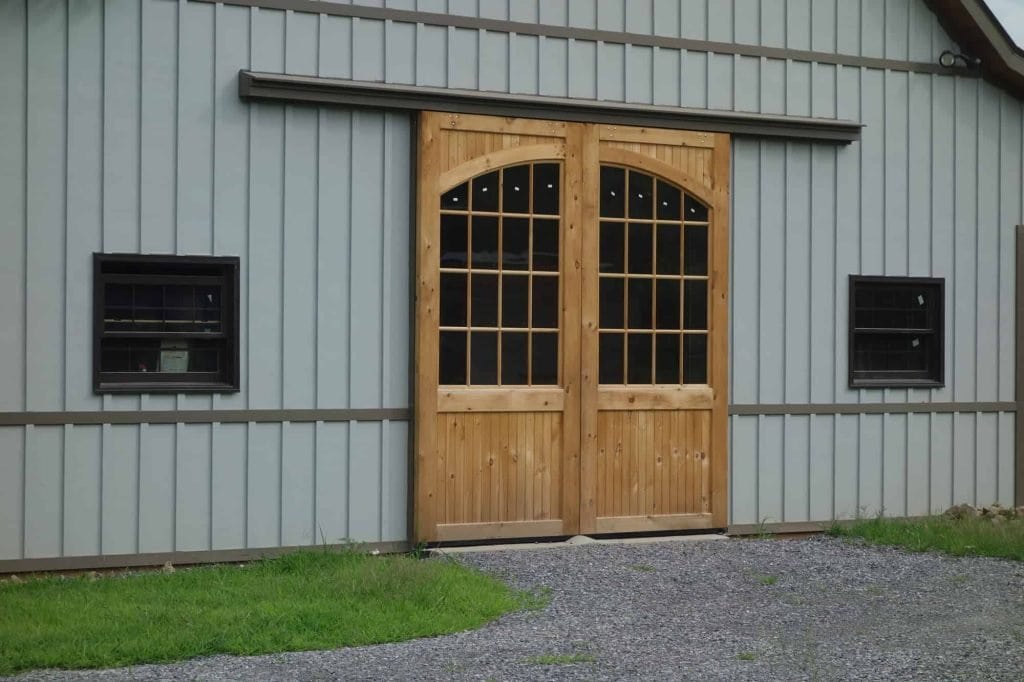 Large wooden barn door on metal building with black windows.