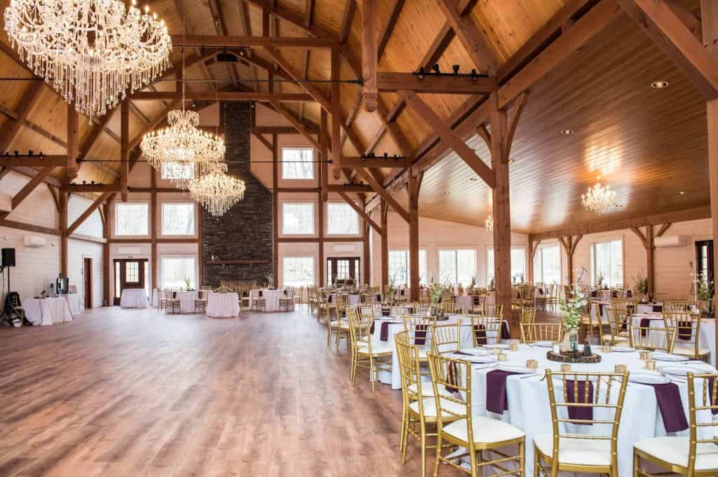 Chandeliers illuminate the spacious wooden event hall with elegant decor and large windows.