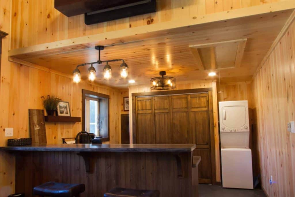 Bright interior shot of a wooden kitchen featuring a washer/dryer, warm wood walls and contemporary lighting.