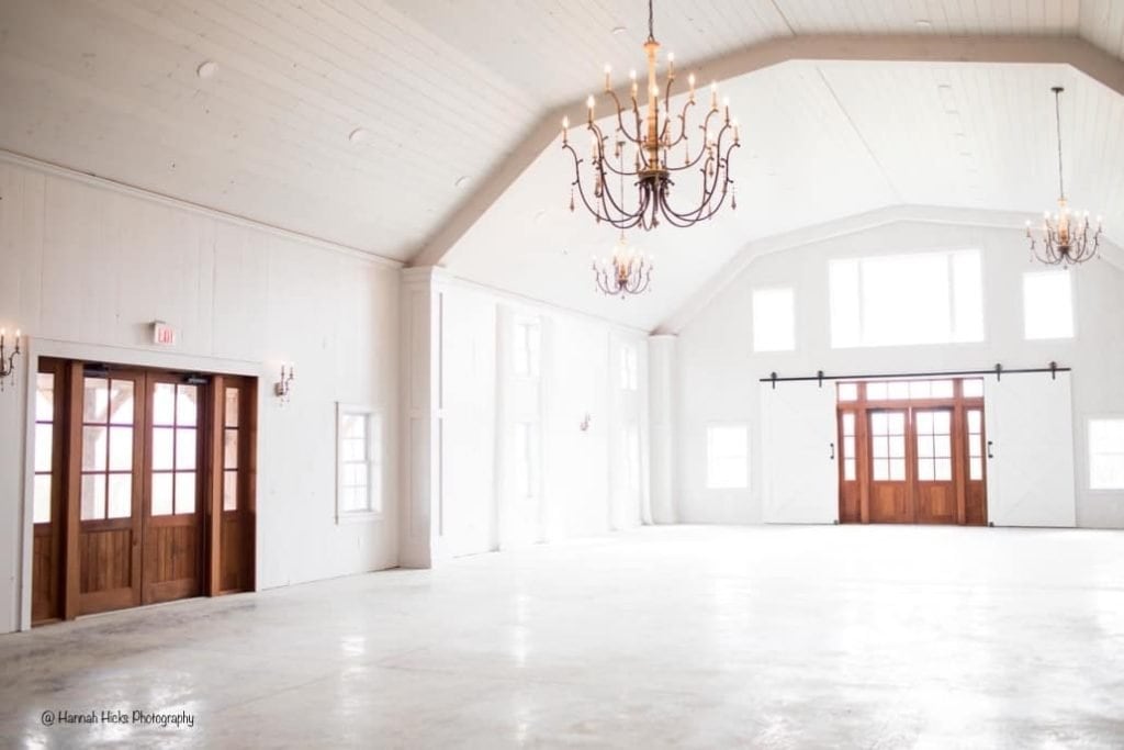 Bright interior of a modern event space with high ceilings, chandeliers, and rustic wooden doors.