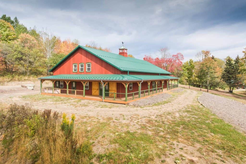 Historic red barn with green roof, large open porch, and fall foliage in the background.