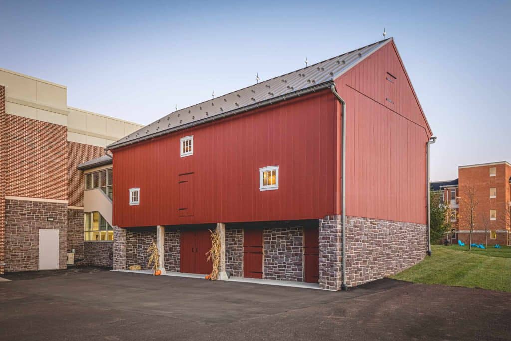 Historic barn renovation featuring red vertical siding and stone foundation by Quarry View Building Group.