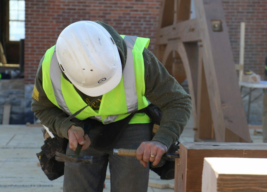 construction worker using hand tools on douglas fir timber to create a timber frame building