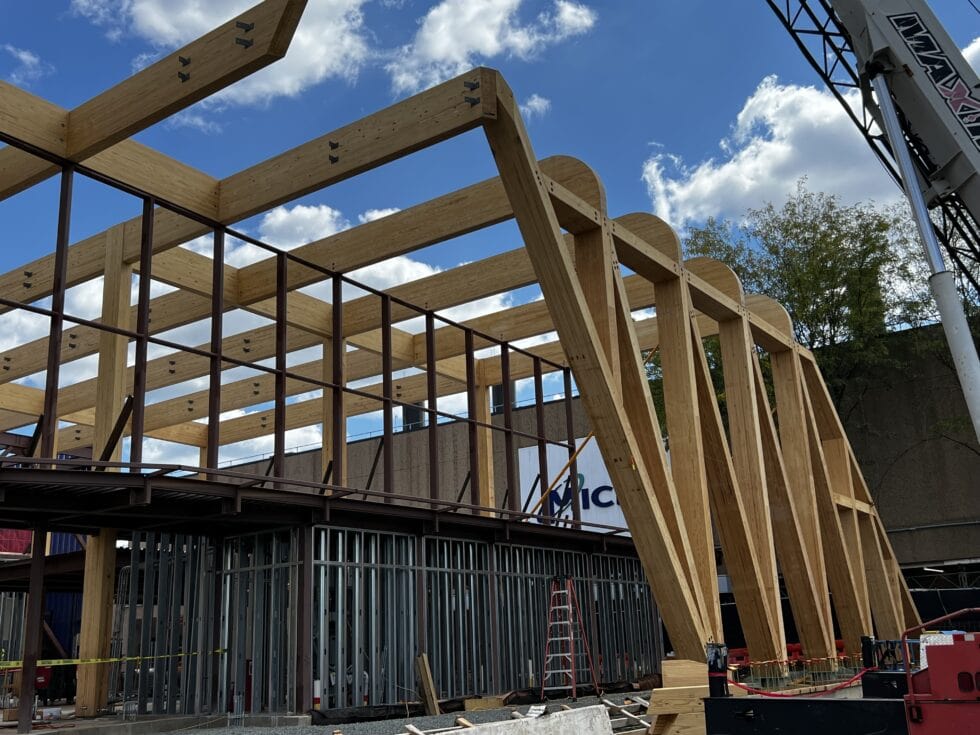 Wooden building framework with large beams and steel supports at construction site.