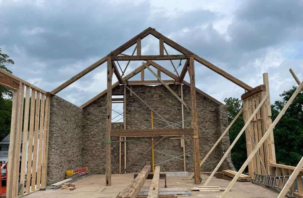 Durable stone wall and new timber roof framing under construction at historic building site.