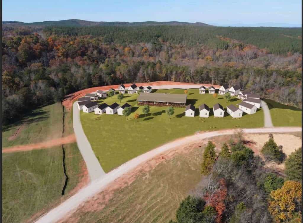 Aerial view of an innovative housing development with white houses, lush green lawns, and surrounding woodland.