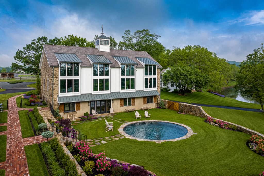 Exterior of a restored historic stone barn in Quakertown, PA, converted into living quarters with modern glass windows, a circular pool, and professional landscaping.
