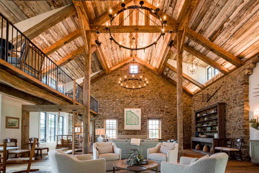Interior of a large residential barn conversion in Quakertown, PA, featuring reclaimed timber framing, original stone walls, two large chandeliers, and a mezzanine level.