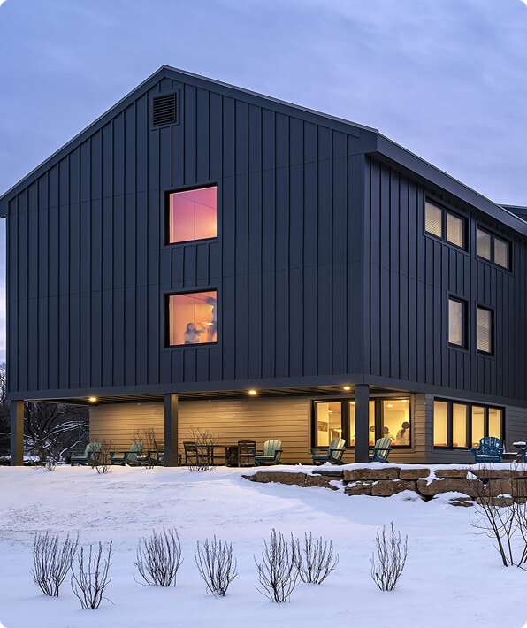 Stunning modern black house with outdoor patio, stylish windows, and snow-covered landscape.