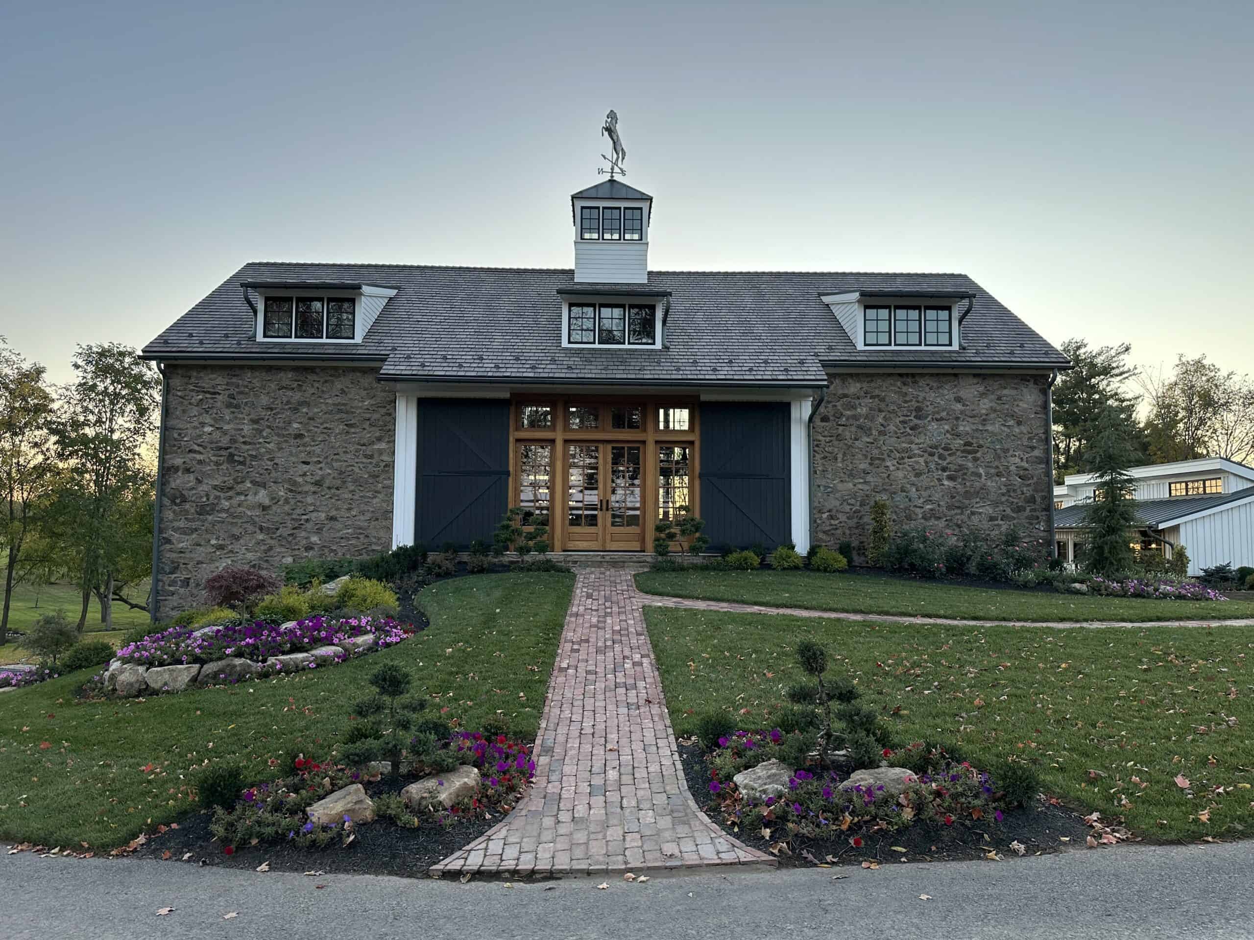 Charming stone barn featuring lush gardens and a brick pathway, ideal for events or rustic home settings.