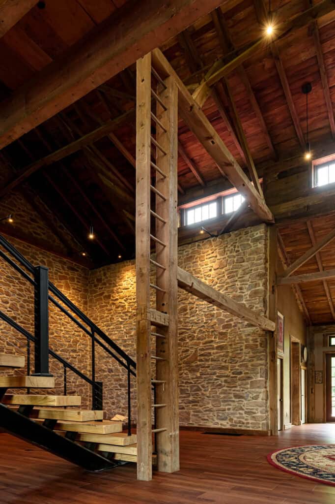Interior of a converted 1832 barn in Blue Bell, PA, featuring original stone walls, a hand-hewn timber ladder post, and a modern floating staircase.