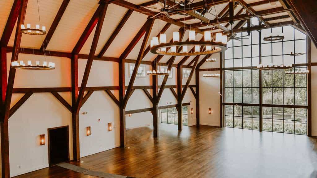 Spacious event hall with high vaulted ceilings, wooden beams, and large windows, perfect for weddings and conferences.