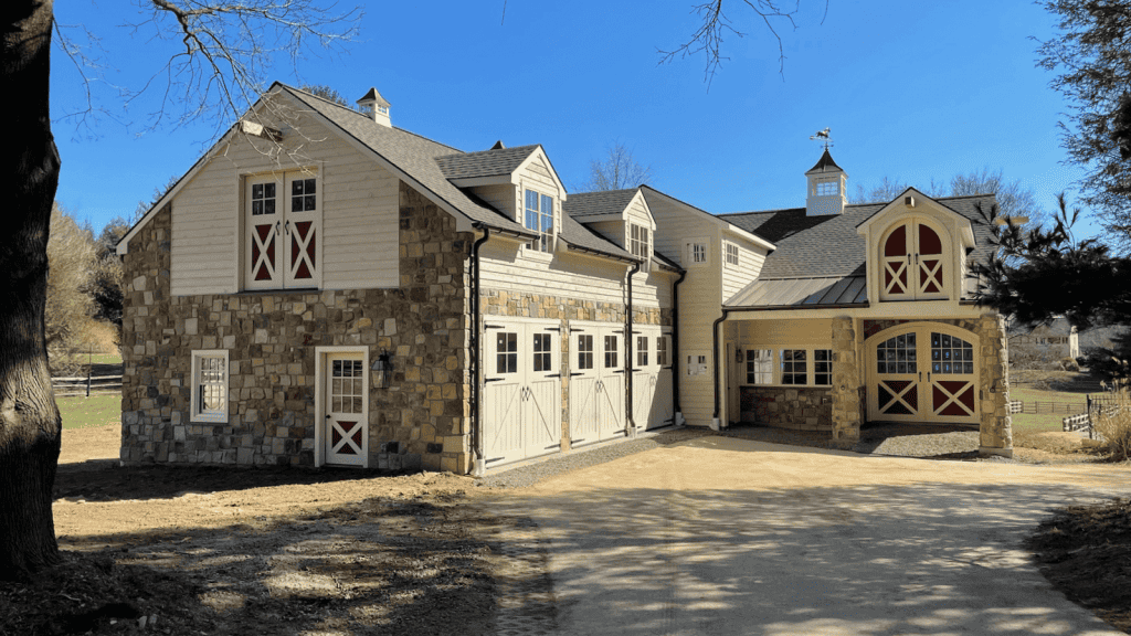 Stunning barn-style house with stone facade and classic barn doors in a scenic rural setting.