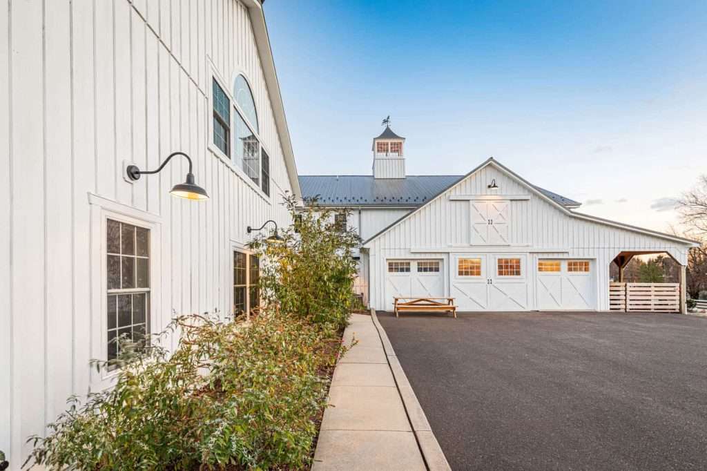 Bright white farmhouse style building with black roof, door, and window accents, featuring expansive windows and outdoor lighting.