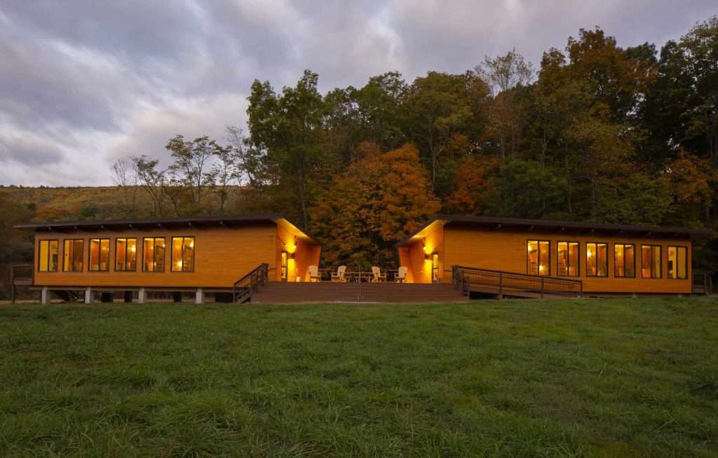 Beautifully crafted timber homes nestled in a lush, wooded landscape during autumn. Warm lighting enhances cozy feel.