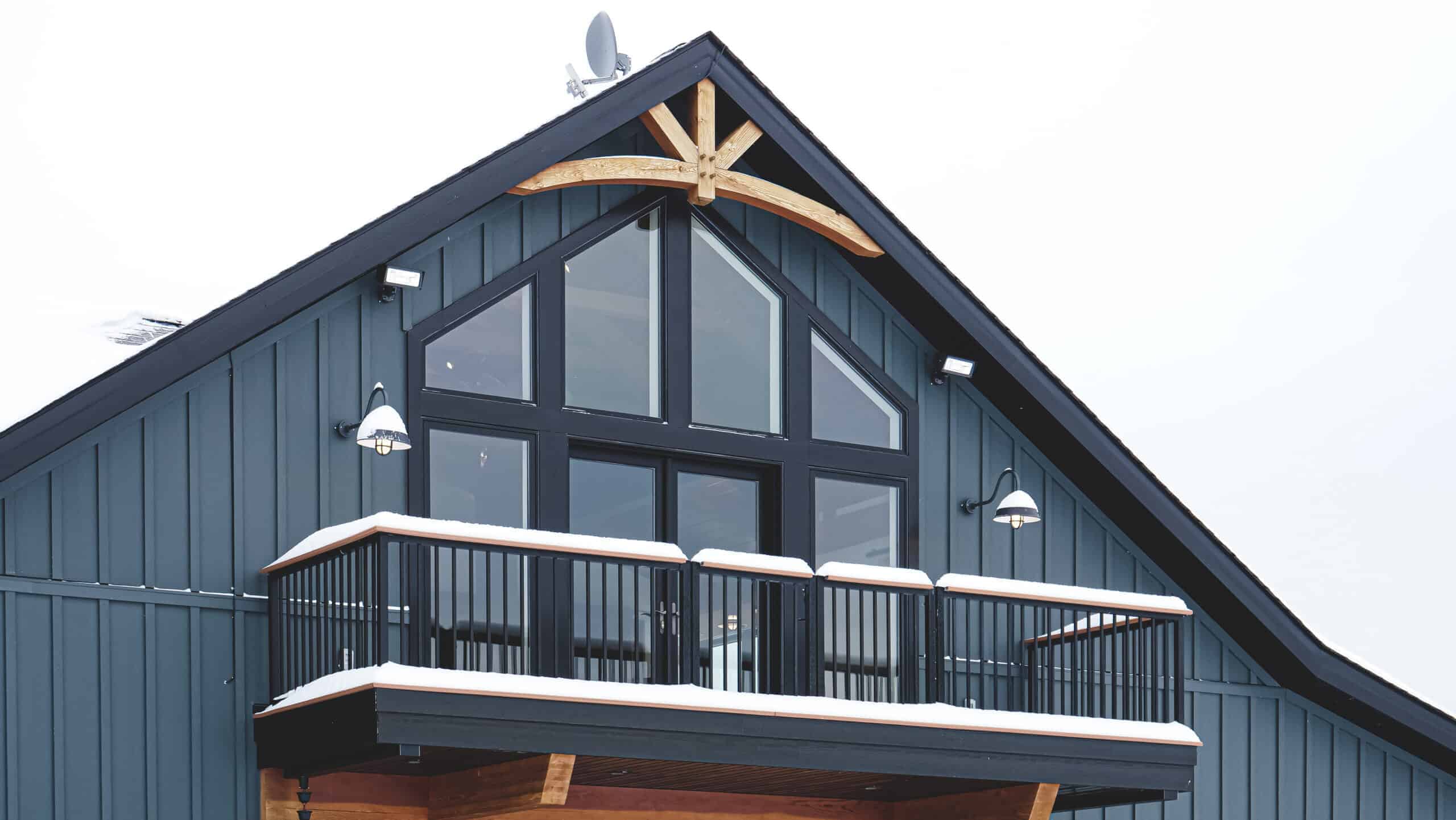 Stylish blue home featuring a balcony, large windows, and snowy roof in a modern design.