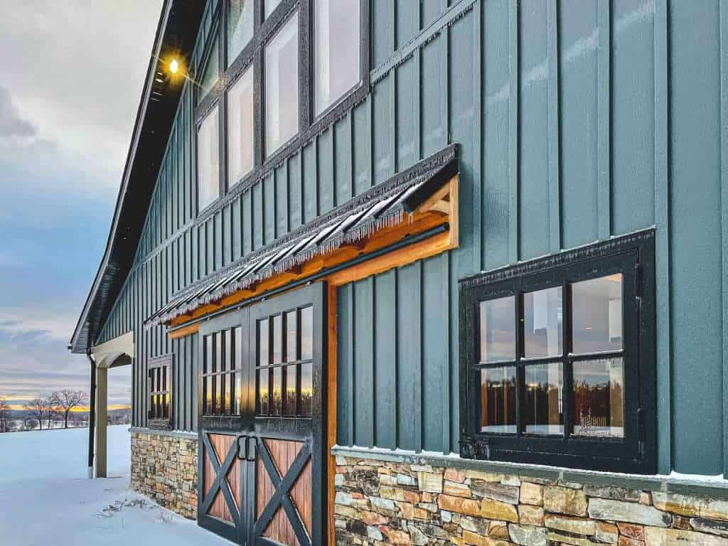 Rustic barn with stone accents, black window frames, and wooden door, part of Quarry View Building Group.