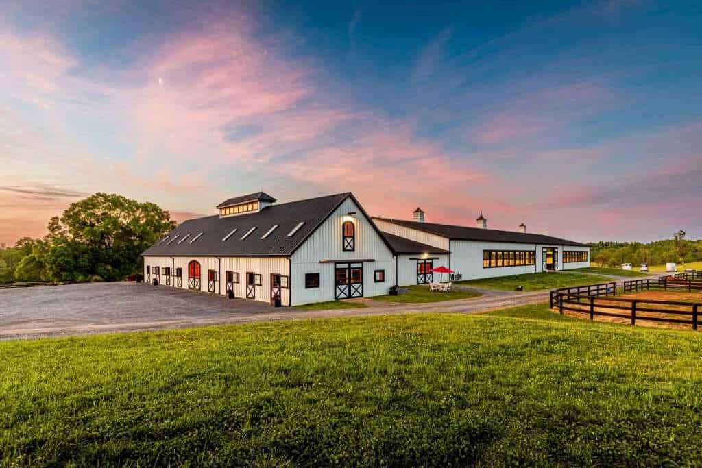 Spacious barn with white siding, black accents, and large windows in a rural landscape.