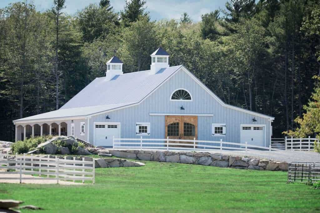 Gorgeous barn-style structure with white siding and wooden doors, nestled in lush greenery, ideal for rustic events.