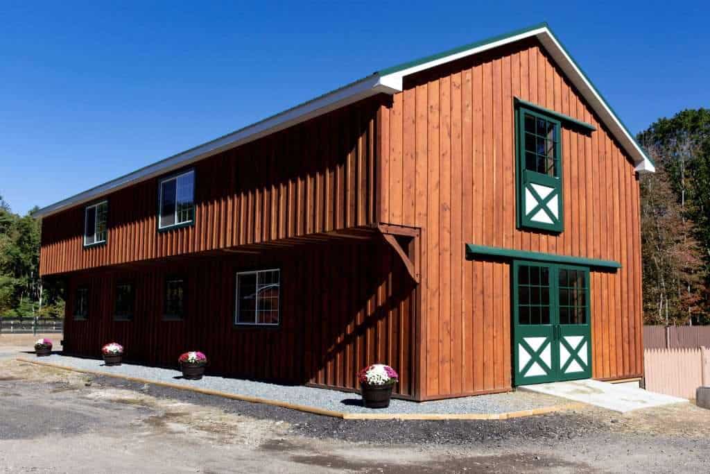 Stylish wooden barn with green trim and large windows, showcasing quality craftsmanship and rural charm.