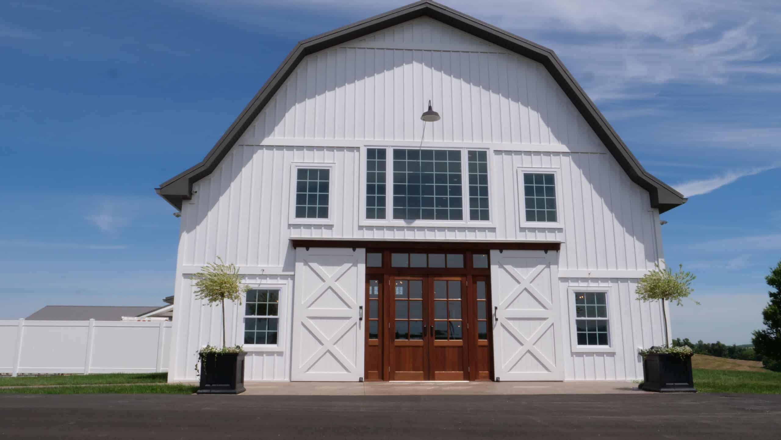 Modern barn building with white exterior, large windows, and wooden double doors in the countryside.