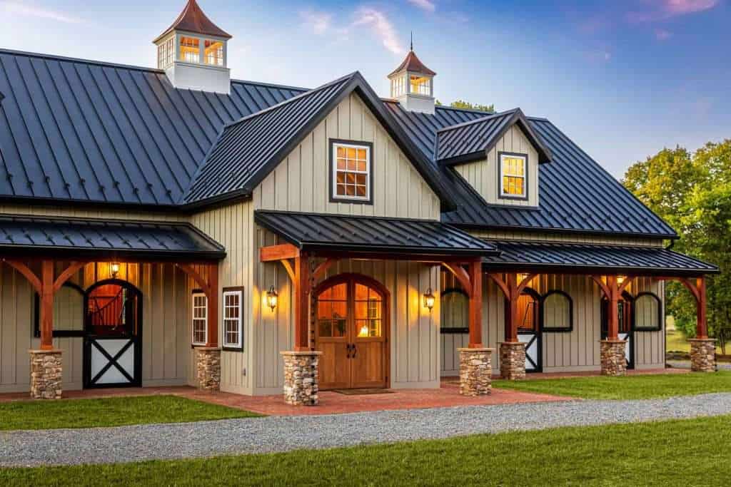 Beautiful barn-style home with metal roof, stone accents, and cozy lighting at sunset.