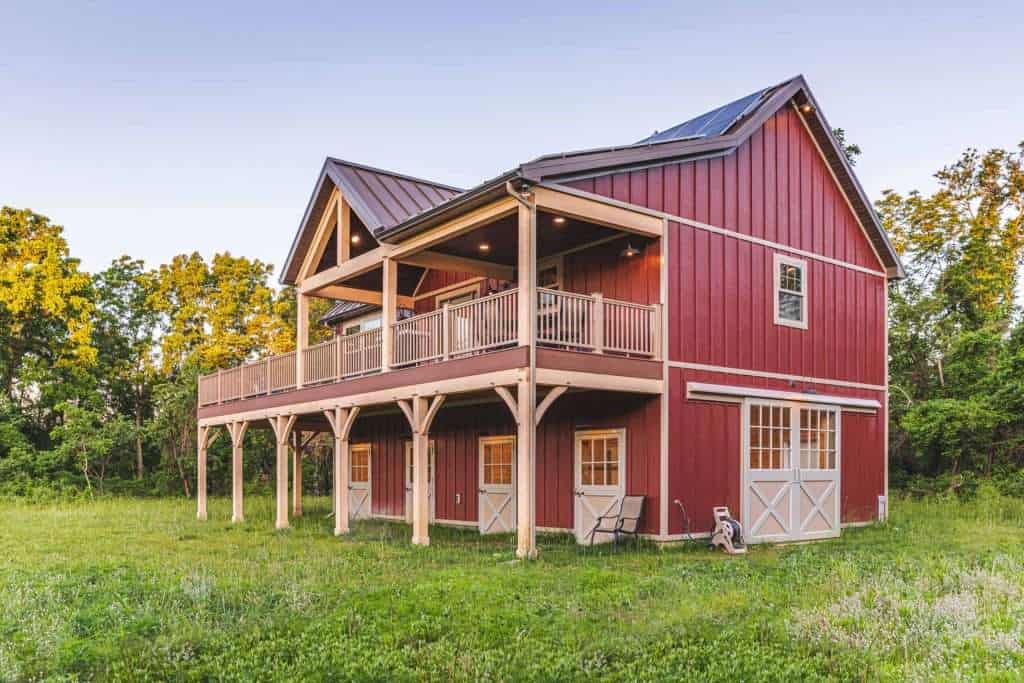 Stylish red barn-style home with large outdoor deck, scenic countryside views, ideal for custom building and rural living.
