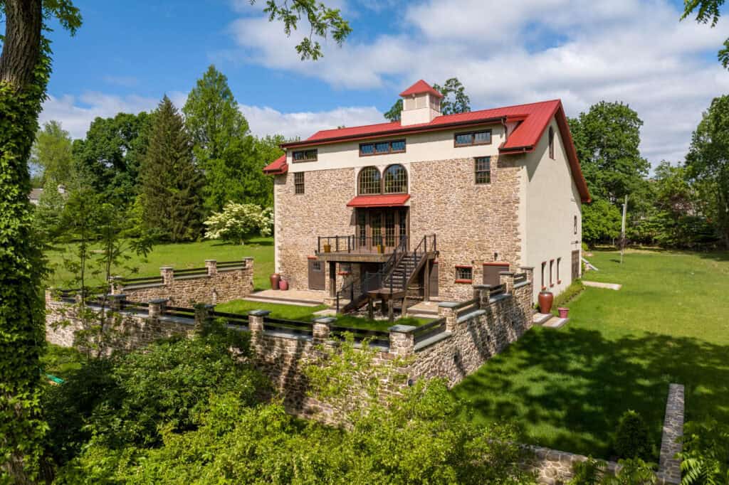 Aerial drone view of a converted 1832 stone barn in Blue Bell, PA, featuring a red metal roof, custom balcony, and a large stone-walled courtyard.