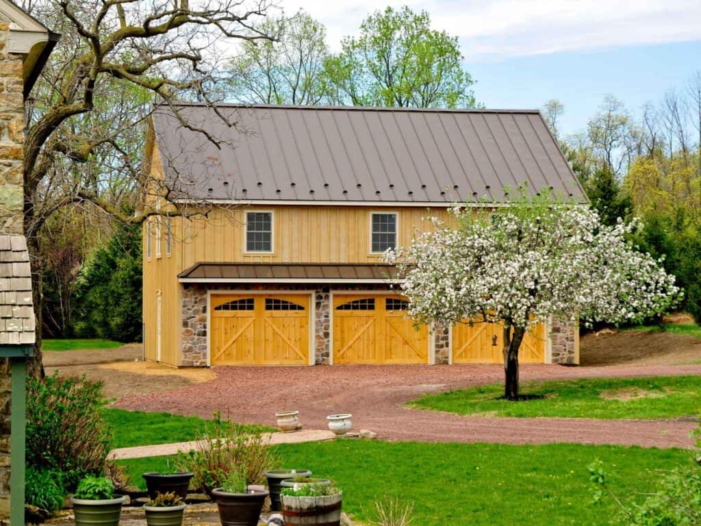 Exterior of a three-car rustic wood garage with natural timber siding and arched wood carriage doors.