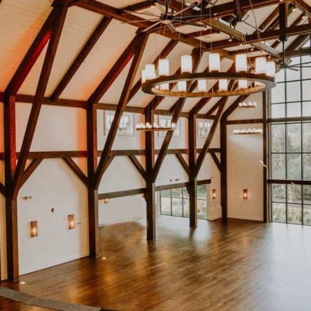 Spacious event hall with high vaulted ceilings, wooden beams, and large windows, perfect for weddings and conferences.